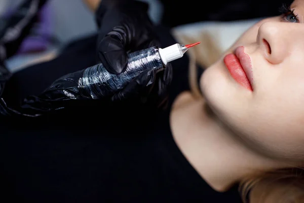 Cosmetologist aplicando tatuagem de maquiagem permanente vermelha em lábios de mulher jovem. Conceito de procedimento de tatuagem de lábios permanentes. — Fotografia de Stock