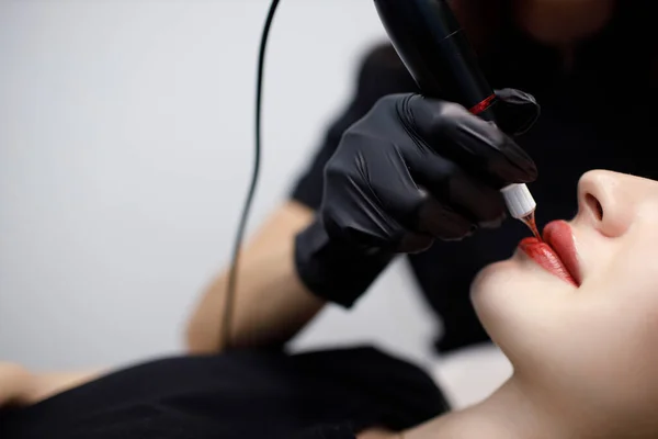 Aplicação de procedimento de tatuagem permanente de pigmento rosa em lábios femininos com máquina de agulha de tatuagem. — Fotografia de Stock