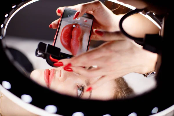Cosmetologist fazendo foto do trabalho no telefone celular vermelho permanente maquiagem tatuagem em lábios de mulher jovem — Fotografia de Stock