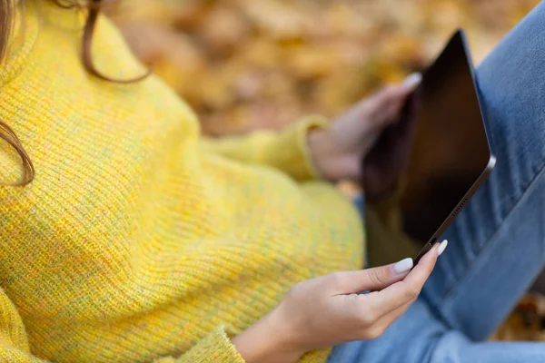 Молодая женщина модель сидит с планшетом Apple iPad Pro 2021 в осеннем парке с желтыми листьями клена. — стоковое фото