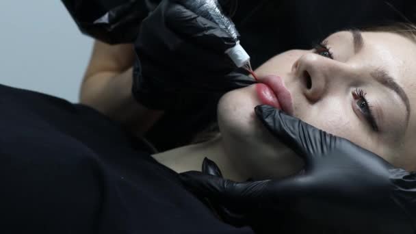 Kosmetolog nanáší růžový pigment permanentní tetování na ženské rty s tetovacím strojem. — Stock video
