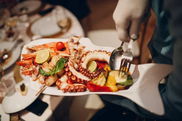 En servitör i en restaurang rymmer skaldjur rätter och serverar ett bord catering koncept hälsosam mat bläckfisk och krabbor skaldjur — Stockfoto