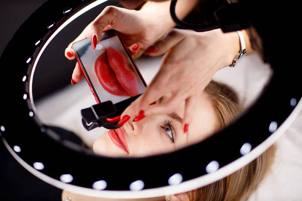 Cosmetologist fazendo foto do trabalho no telefone celular vermelho permanente maquiagem tatuagem em lábios de mulher jovem — Fotografia de Stock