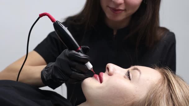 Cosmetologist aplicando tatuagem permanente de pigmento rosa em lábios femininos com máquina de agulha de tatuagem. — Vídeo de Stock