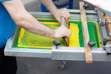 Giyim fabrikasında seri ipek ekran baskı işlemi. Çerçeve, cam sileceği ve plastisol rengi