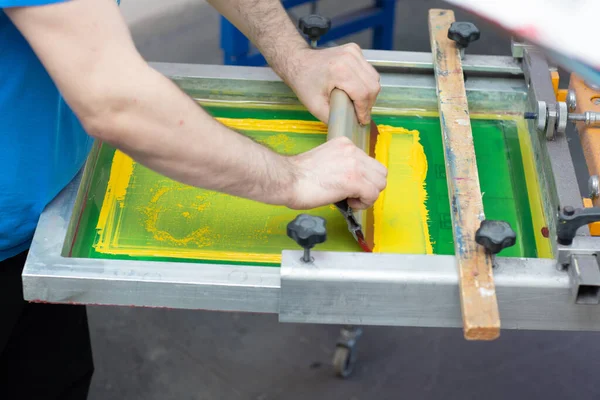 Serigrafie zeefdruk proces in de kledingfabriek. Frame, squeegee en plastisol verven — Stockfoto