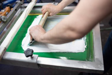 Giyim fabrikasında seri ipek ekran baskı işlemi. Çerçeve, cam sileceği ve plastisol rengi