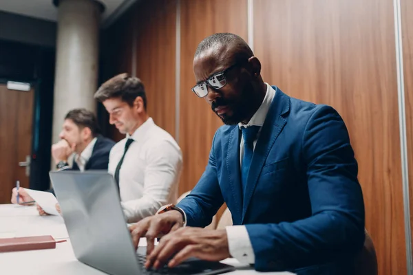 Afrykański czarny mężczyzna biznesmen siedzi przy stole z laptopem w biurze zespół ludzi tło. — Zdjęcie stockowe