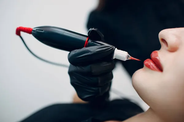 Cosmetologist aplicando tatuagem de maquiagem permanente vermelha em lábios de mulher jovem — Fotografia de Stock
