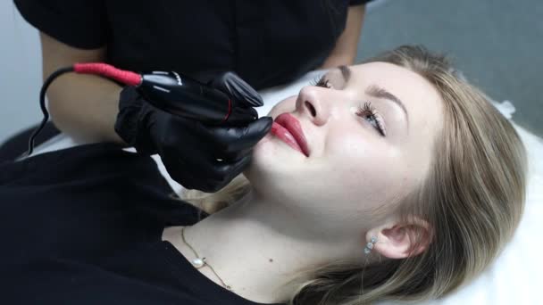 Cosmetólogo aplicando pigmento rosa tatuaje permanente en labios femeninos con máquina de aguja de tatuaje. — Vídeos de Stock