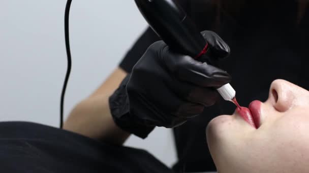 Cosmetologist appliquant le tatouage permanent de pigment rose sur les lèvres femelles avec la machine à tatouer d'aiguille. — Video