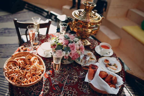 Mesa tradicional rusa para tomar té con un samovar, copas de vino, flores, pasteles, rosquillas y bollos — Foto de Stock