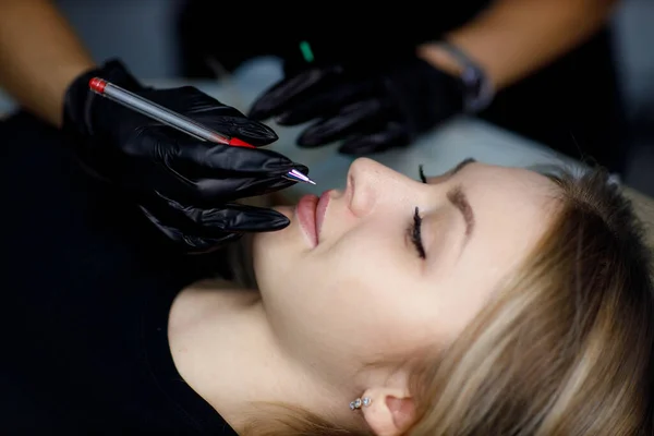 Cosmetologist aplicando o contorno de desenho no lábio antes de fazer o procedimento de tatuagem microblading dos lábios — Fotografia de Stock