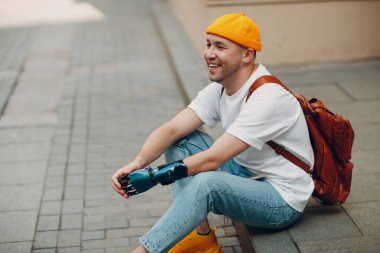 Yapay eli olan engelli genç adam kaldırımda oturuyor ve gülüyor..