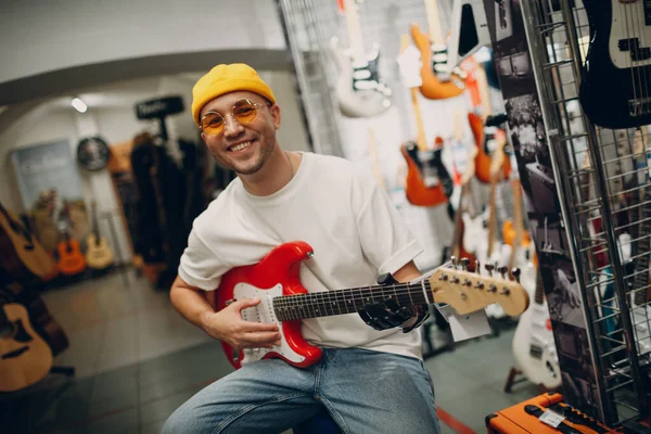 Pemuda cacat dengan tangan buatan bermain gitar di toko. — Stok Foto