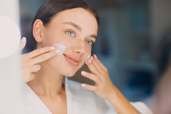 Молодая женщина нанесла косметический белый крем на лицо