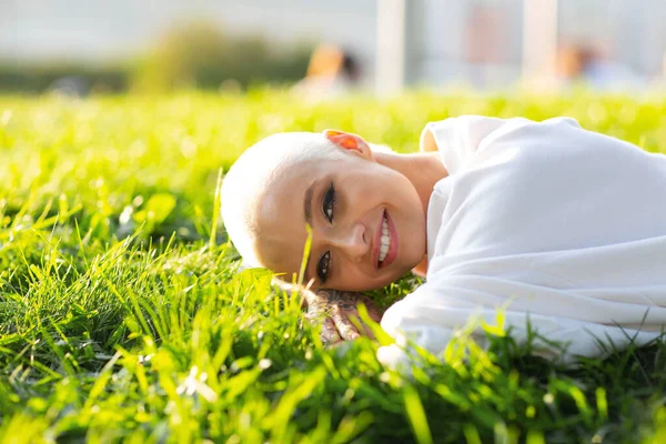 Wanita muda Millenial berambut pendek di luar ruangan tersenyum berbaring di atas potret rumput. Stok Gambar Bebas Royalti