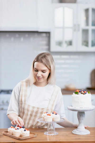 Koki kue manis wanita muda kaukasia dengan kue di meja dapur. — Stok Foto