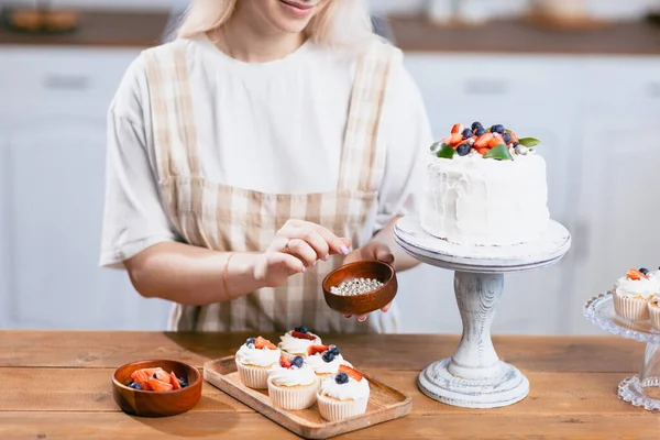 Koki kue manis wanita muda kaukasia dengan kue di meja dapur. — Stok Foto