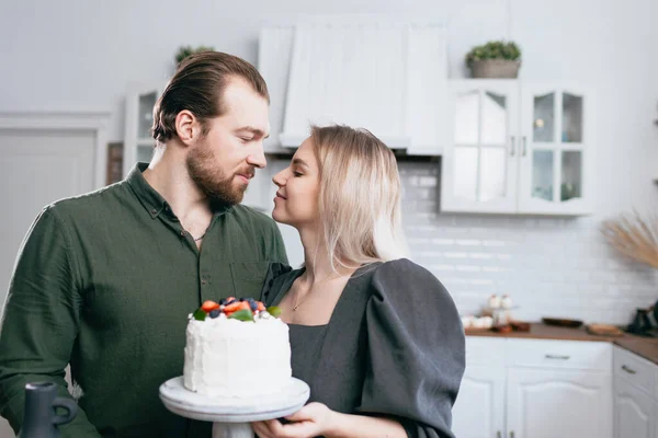 Cukiernik cukiernik młoda kaukaska kobieta z mężem chłopak mężczyzna spróbować smaku tortu na stole w kuchni. Ciastka babeczki i słodki deser. — Zdjęcie stockowe