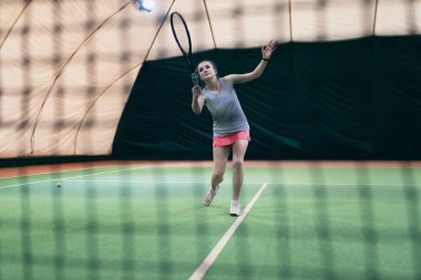 Tenisçi kadın oyuncu mahkemede raket ve topla antrenman yapıyor.