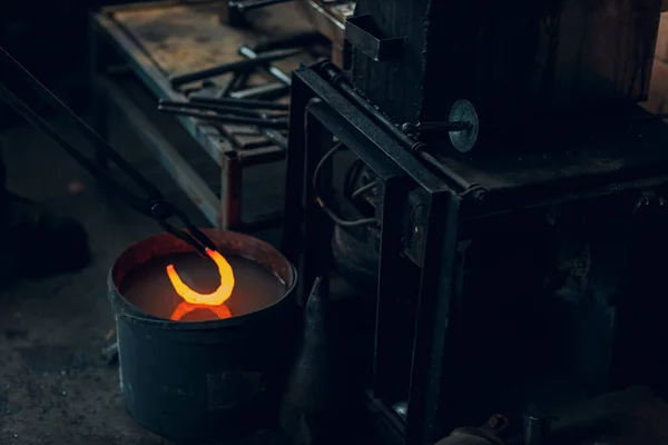 铁匠锻造金属马蹄铁并在铁罐中加水调质 — 图库照片