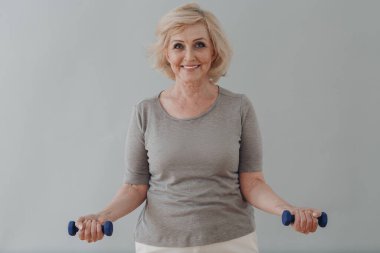 Yaşlı, beyaz, yaşlı kadın portresi gri saçlı, dambıllarla egzersiz yapıyor..