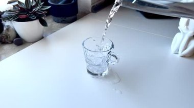 Su şeffaf bir bardağa dökülür, ağır çekimde.