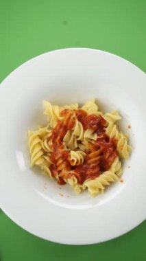 Parmesan peyniri kırmızı arka plandaki bir tabakta makarnanın üzerine düşer.