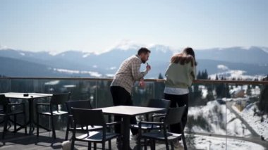 Bir erkek ve bir kız dağlara bakan terasta sohbet ediyorlar.