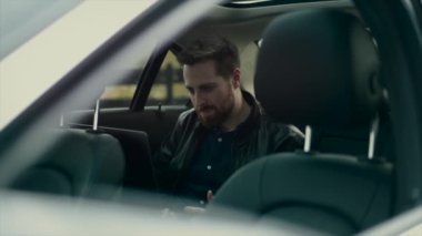 Arka koltukta oturan bir adam bilgisayarda çalışıyor ve çok mutlu.