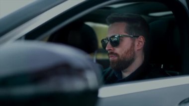 İş adamı arabada telefonla konuşur, arabanın kapısından bakar.