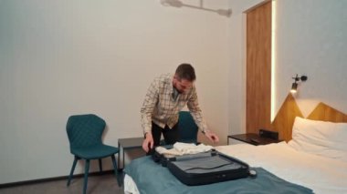 Genç bir adam giysilerini bavuldan çıkarıyor.