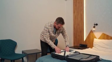 Genç bir adam giysilerini bavuldan çıkarıyor.