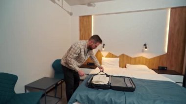 Genç bir adam giysilerini bavuldan çıkarıyor.