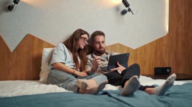 young couple watching video on tablet in hotel room and smiling