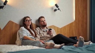 Genç çift otel odasında televizyon izliyor ve gülümsüyor.