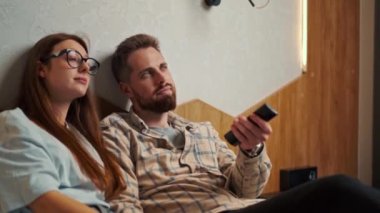 Genç çift otel odasında televizyon izliyor ve gülümsüyor.