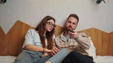 young couple watching TV in hotel room calmly