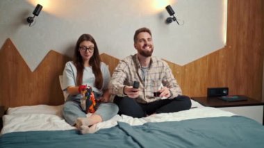 young couple watching football in hotel room with chips