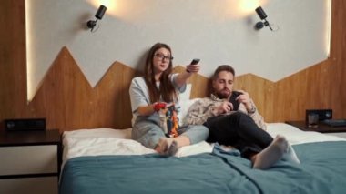 Genç çift otel odasında televizyon izliyor ve gülümsüyor.