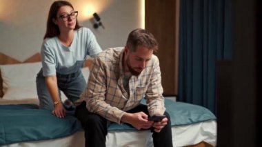 the guy works on the phone in the hotel room and the girl requires attention for love