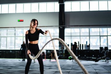 Güçlü bir kadın, karanlık spor salonunda kardiyo antrenmanında dövüş ipleri eğitiyor. Profesyonel atlet spor salonu ekipmanları. Güçlü vücut geliştirici ağırlık kaldırıyor. Atletik kişi çabası