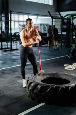 Güçlü bir adam jimnastik salonunda çekiç kullanıyor. Kaslı bir adam balyozla büyük bir lastiğe çarpıyor. Spor kulübünde yoğun antrenman yapan güçlü bir sporcu. Silüet atlet egzersizi