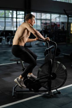 Genç Atletik orta yaşlı adam hava direnci bisikleti eğitimi, spor salonunda çapraz antrenman seti. Spor salonunda spor ayakkabılarıyla bisiklet süren aktif bir adam. Hava bisikletinde erkek eğitimi.