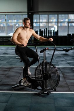 Genç Atletik orta yaşlı adam hava direnci bisikleti eğitimi, spor salonunda çapraz antrenman seti. Spor salonunda spor ayakkabılarıyla bisiklet süren aktif bir adam. Hava bisikletinde erkek eğitimi.