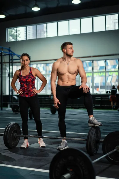 Exhausted men and women resting after intensive workout in gym. Fitness healthy man and woman tired after strength training exercise at gym. Tired male and female standing and relaxing after intense workout.