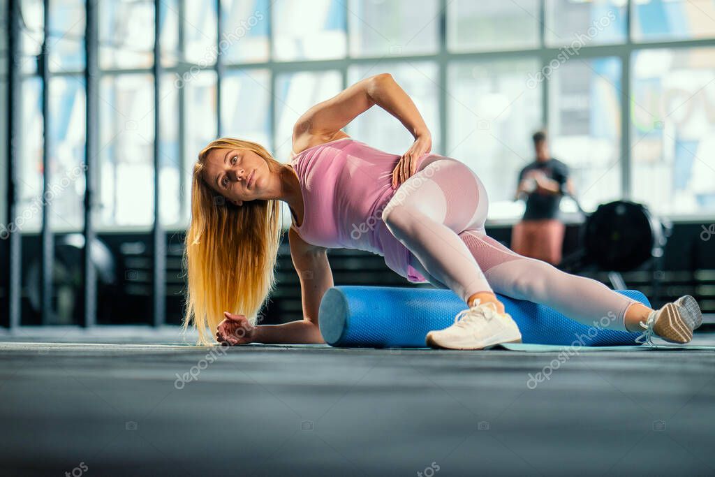 Woman athlete rolls muscles on a karemat in the gym, doing stretching