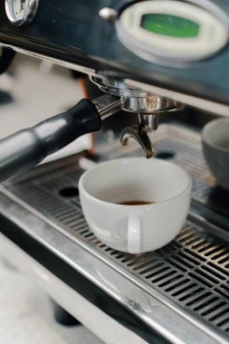 Profesyonel bir makineden bir fincana kahve dökülüyor. Kahveci filtre tutacağı kullanarak duble espresso yapıyor. Taze kahve akıyor. Sabahları kavrulmuş sade kahve içmek.