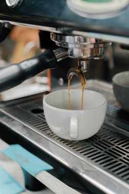 Profesyonel bir makineden bir fincana kahve dökülüyor. Kahveci filtre tutacağı kullanarak duble espresso yapıyor. Taze kahve akıyor. Sabahları kavrulmuş sade kahve içmek.